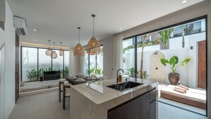 A modern kitchen with a large island, pendant lights, and a view of the outdoors. - Nova Oasis 1 (Canggu)