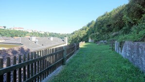 A grassy pathway bordered by a wooden fence, leading to a stone wall and dense greenery. - Vacation apartment with an excellent view (Ach)
