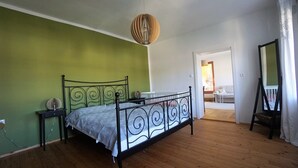 A bedroom with a metal bed frame, a green wall, a wooden floor, a hanging light fixture, and a view of a balcony with a chair and a table. - Vacation apartment with an excellent view (Ach)