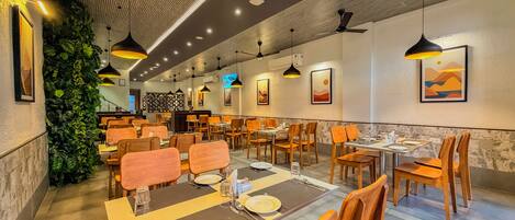 A restaurant with multiple dining tables and chairs, ceiling fans, and wall-mounted artwork.
