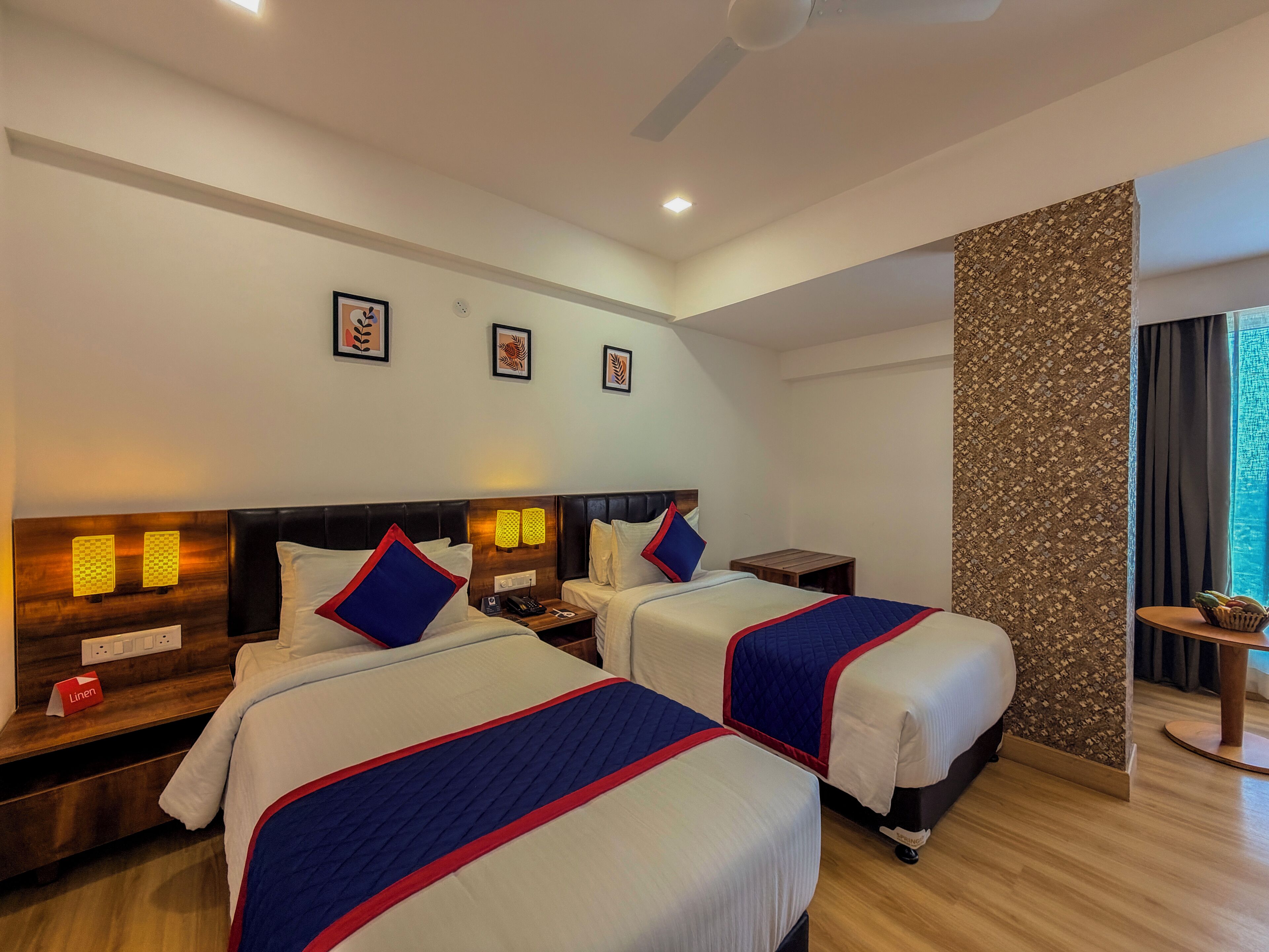 Una habitación de hotel con dos camas, un cabecero de madera, una mesita pequeña y un panel decorativo en la pared.