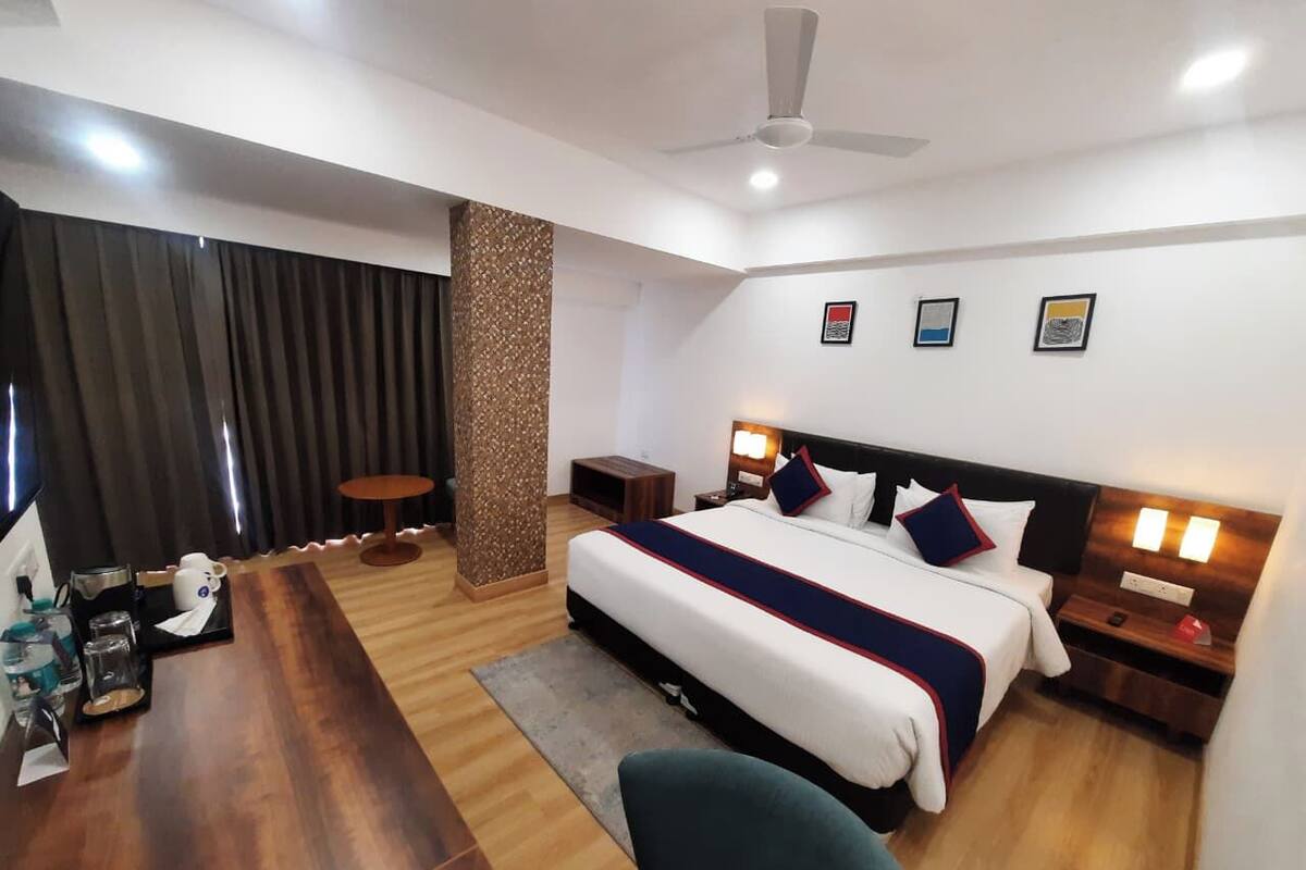 A hotel room with a bed, bedside tables, a desk, a chair, a coffee machine, and a TV.