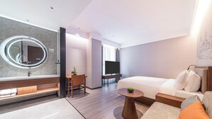 A modern hotel room with a large round mirror, a sofa, a small table, a TV, and a desk with a chair. - UrCove by Hyatt Lanzhou Xiguan Cross Zhongshan Bridge (Lanzhou)