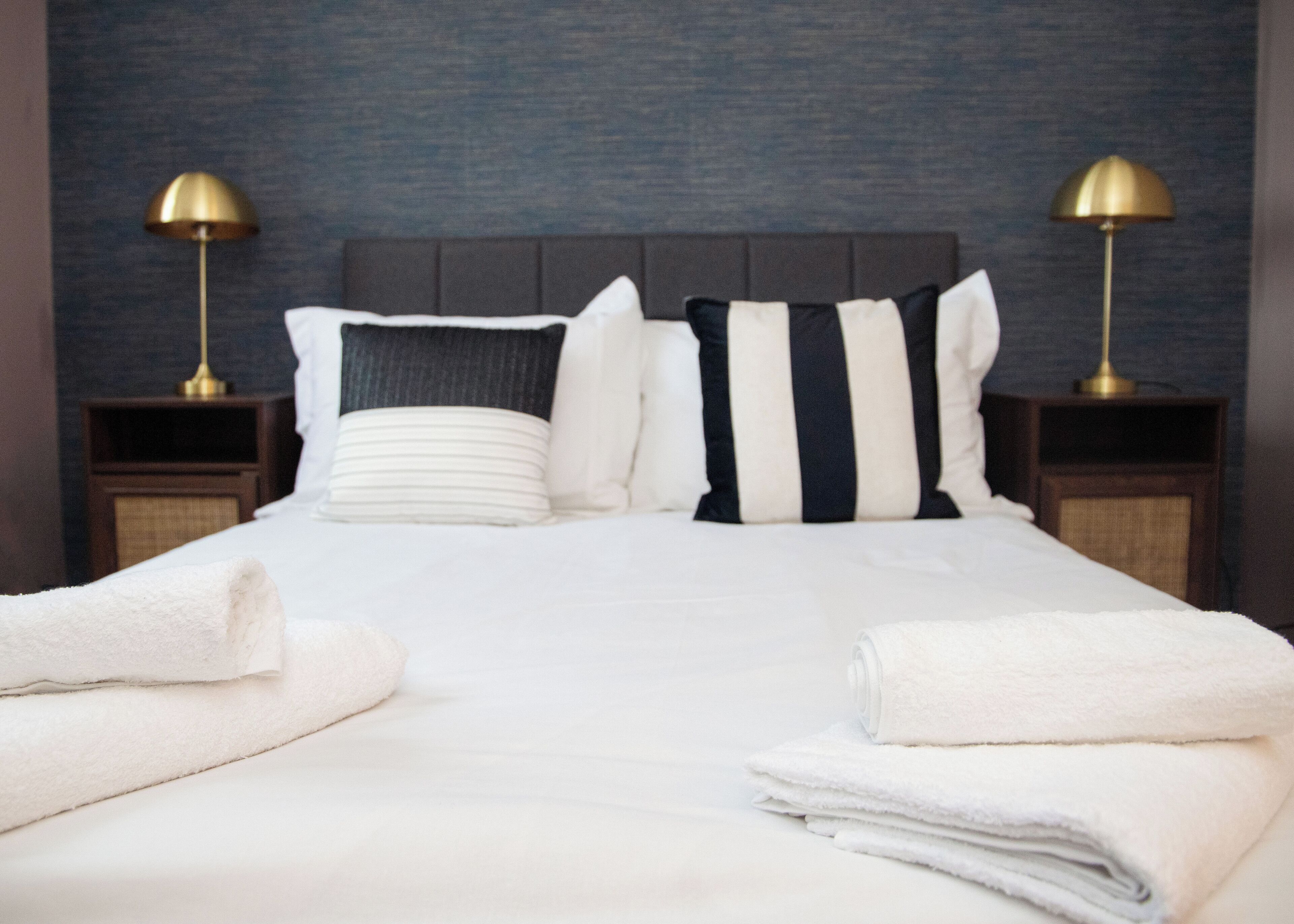 A neatly made bed with striped pillows, a folded white towel, and two bedside lamps on wooden nightstands.