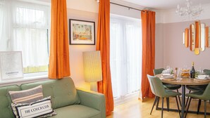 Un coin repas avec une table ronde dressée pour quatre personnes, un canapé agrémenté d’un coussin sur lequel est inscrit « THE COUCH CLUB », et un tableau encadré accroché au mur.