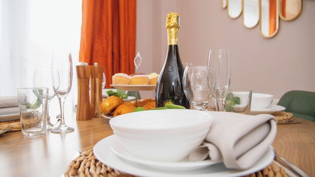 Une table à manger dressée avec des assiettes, des verres, une bouteille de champagne et des pâtisseries.