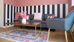 Una sala de estar con un sofá, un sillón azul, una mesa de centro y una alfombra estampada.