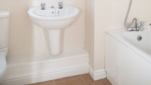 Un baño con lavamanos pedestal, ventana, bañera y retrete.