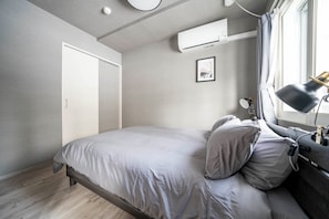 A modern bedroom with a bed, bedside lamp, and an air conditioning unit. - COURT VILLA SAPPORO 102 (Sapporo)