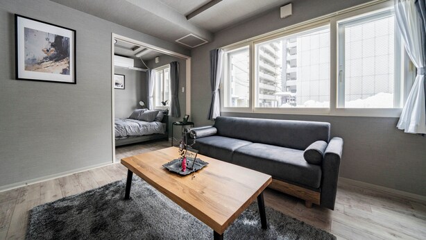 A modern living room with a wooden coffee table, grey sofa, and large windows. - COURT VILLA SAPPORO 102 (Sapporo)