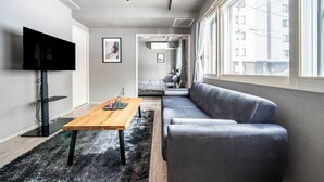 A modern living room with a wooden coffee table, grey sofa, and a flat-screen TV mounted on the wall. - COURT VILLA SAPPORO 102 (Sapporo)
