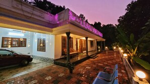 A building with a covered porch, a car parked in front, and a brick pathway leading to the entrance. - A one Cottage Munnar (Anachal)