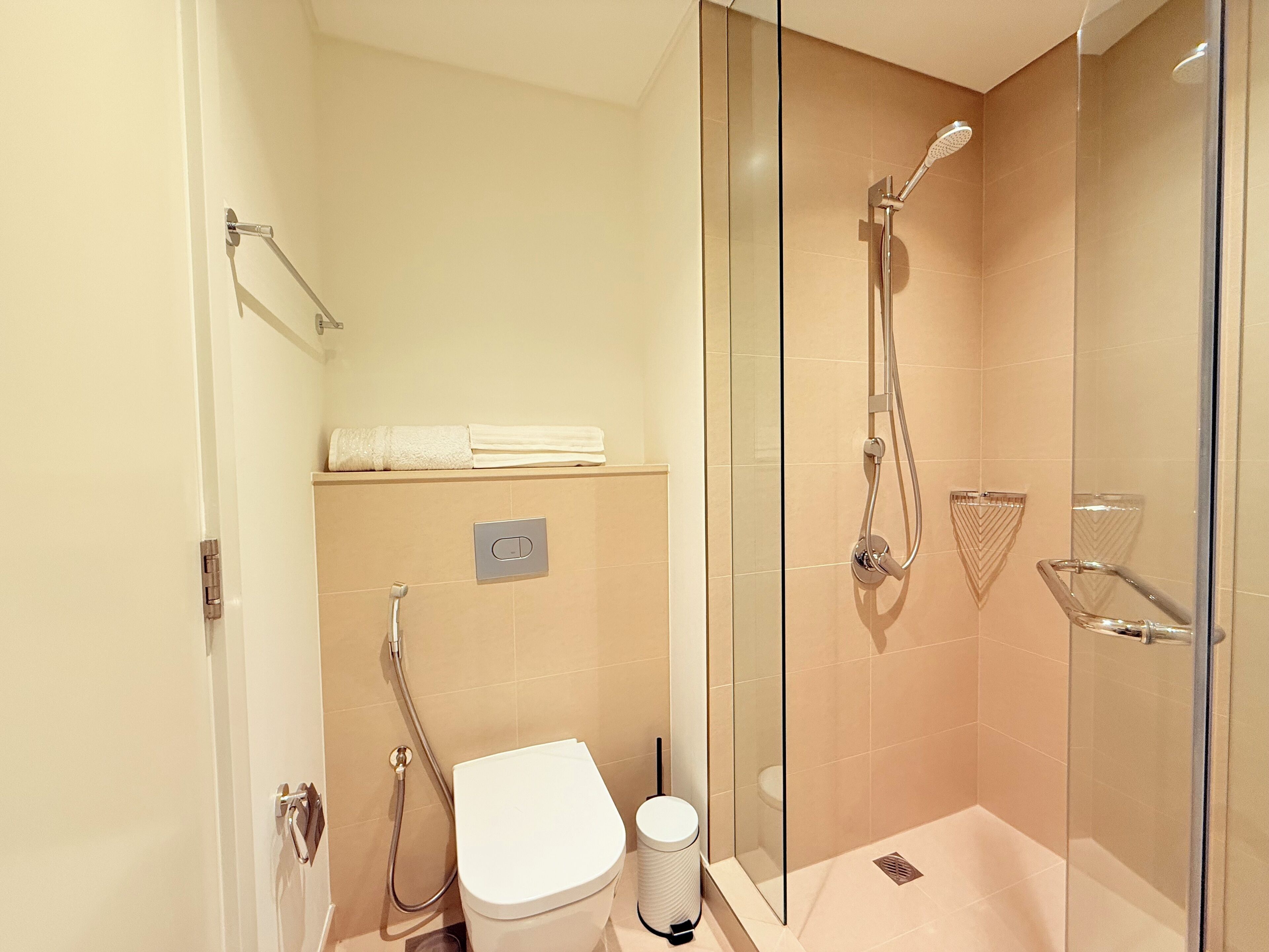 Een moderne badkamer met een douche met glazen wand, een toilet en een handdoekhouder.