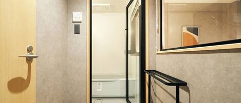 A hallway with a wooden door, a glass door leading to a bathroom, and a black metal bench.