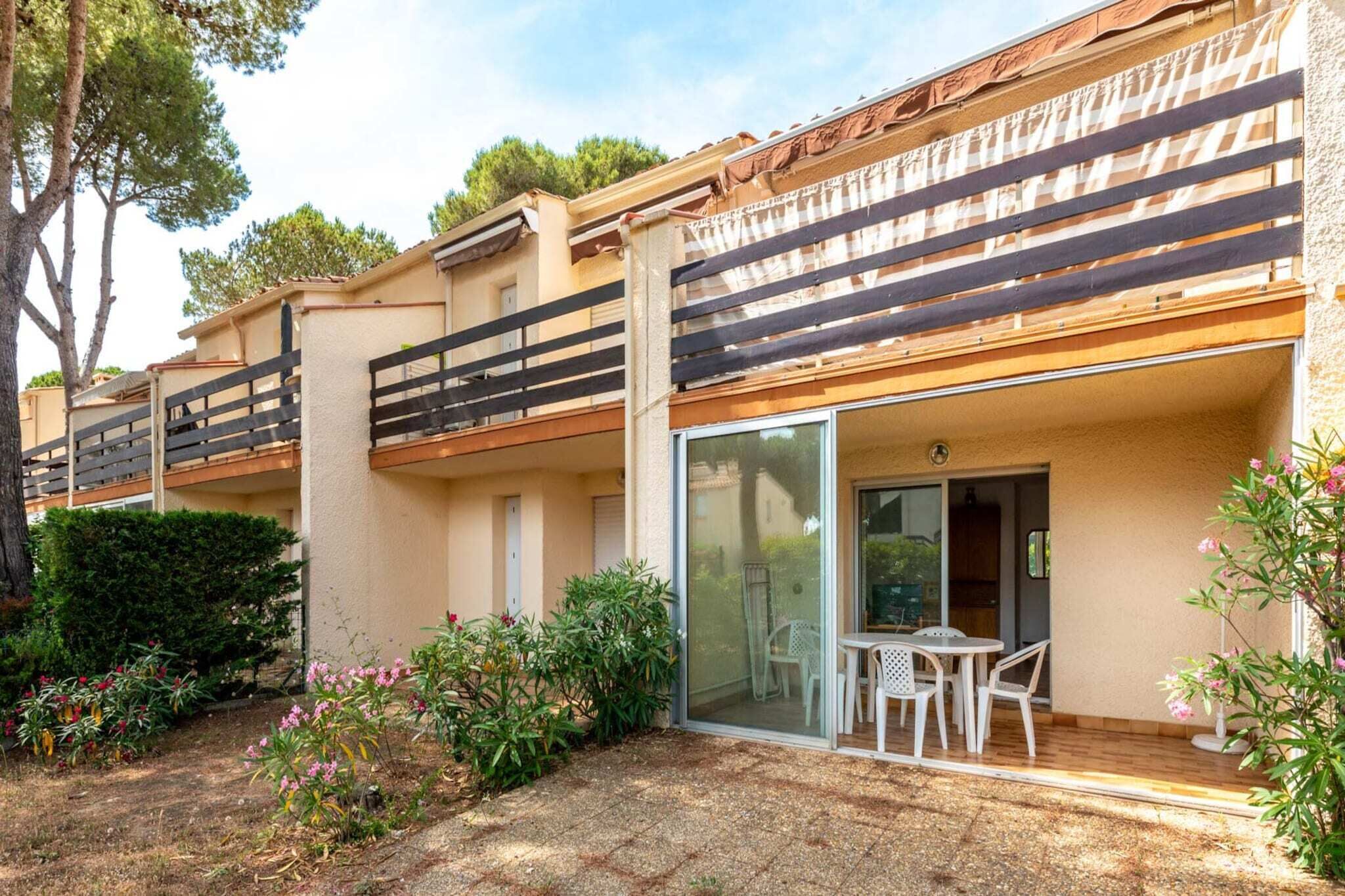 A residential building with balconies, a patio area with a table and chairs, and a garden with various plants.