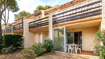 A residential building with balconies, a patio area with a table and chairs, and a garden with various plants.