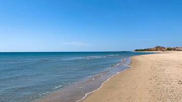 A beach with clear blue water, a sandy shore, and a distant town.
