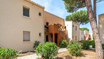A row of Mediterranean-style buildings with terracotta roofs, a stone pathway, and lush greenery.
