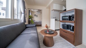 A modern living room with a grey sofa, a round wooden coffee table, and a built-in kitchen unit with a microwave and coffee maker. - COURT VILLA SAPPORO 403 (Sapporo)