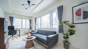 A modern living room with a grey sofa, a round coffee table, a potted plant, and a framed abstract artwork on the wall. - COURT VILLA SAPPORO 403 (Sapporo)