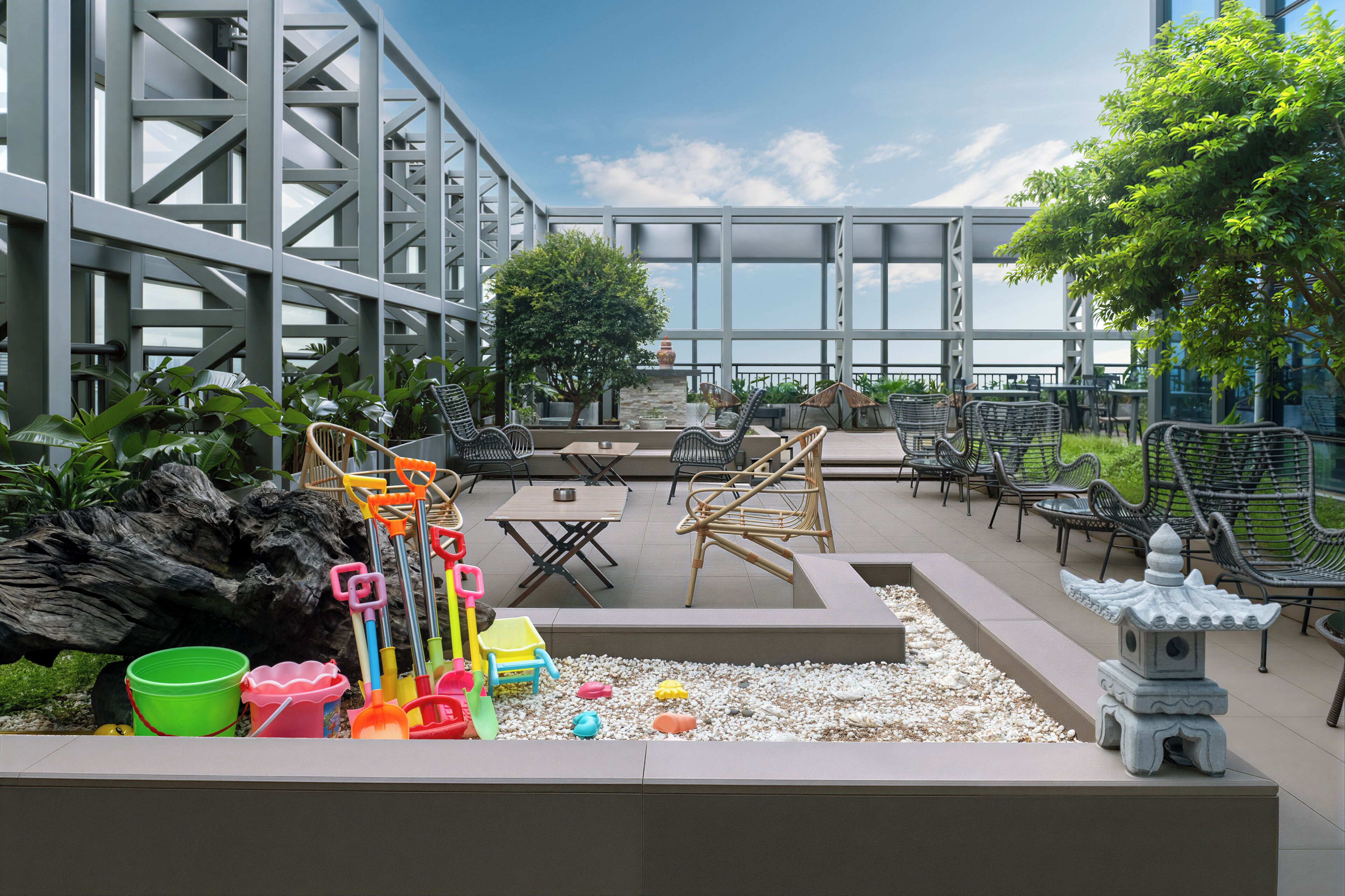 An outdoor seating area with tables and chairs, a small garden with pebbles, and a decorative stone structure.