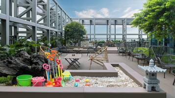 An outdoor seating area with tables and chairs, a small garden with pebbles, and a decorative stone structure.