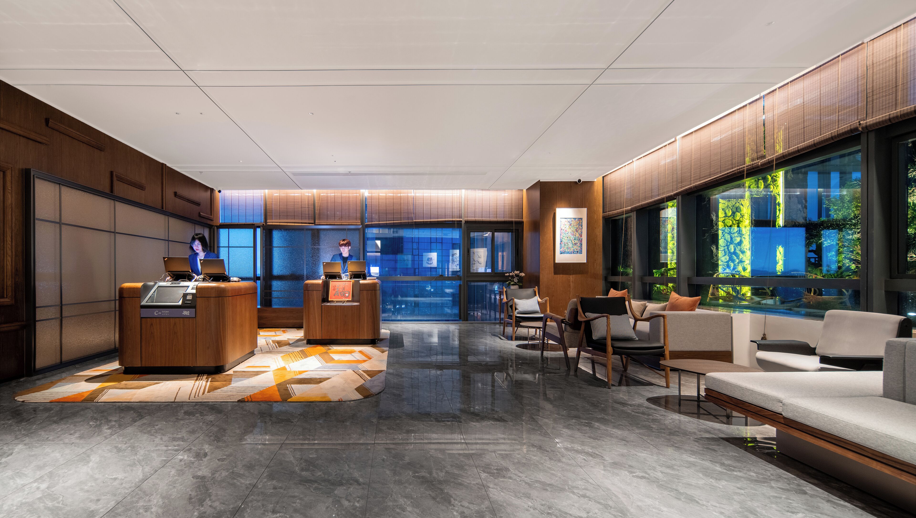 A modern lobby with wooden paneling, a reception desk, seating area, and large windows with a view of greenery.