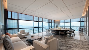 Un salón espacioso con techo alto, ventanas grandes que ofrecen vistas a la ciudad, una zona de comedor con mesa redonda y muebles modernos.