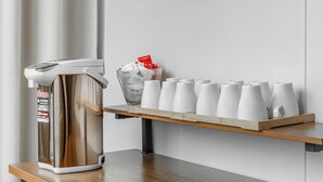 En kaffemaskine og et fad med hvide kopper på et træbord.