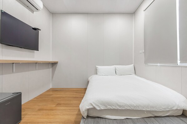 A modern bedroom with a bed, a flat-screen TV mounted on the wall, and a wooden floor. - Muij (Liuqiu)