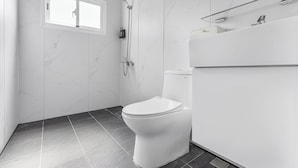 Et moderne badeværelse med toilet, brusebad og et vindue.
