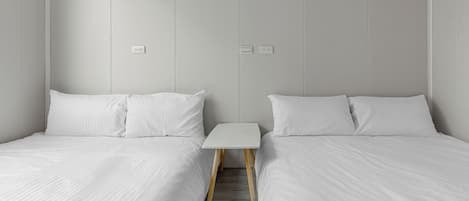 A hotel room with two single beds, a small white table, and a wooden floor.