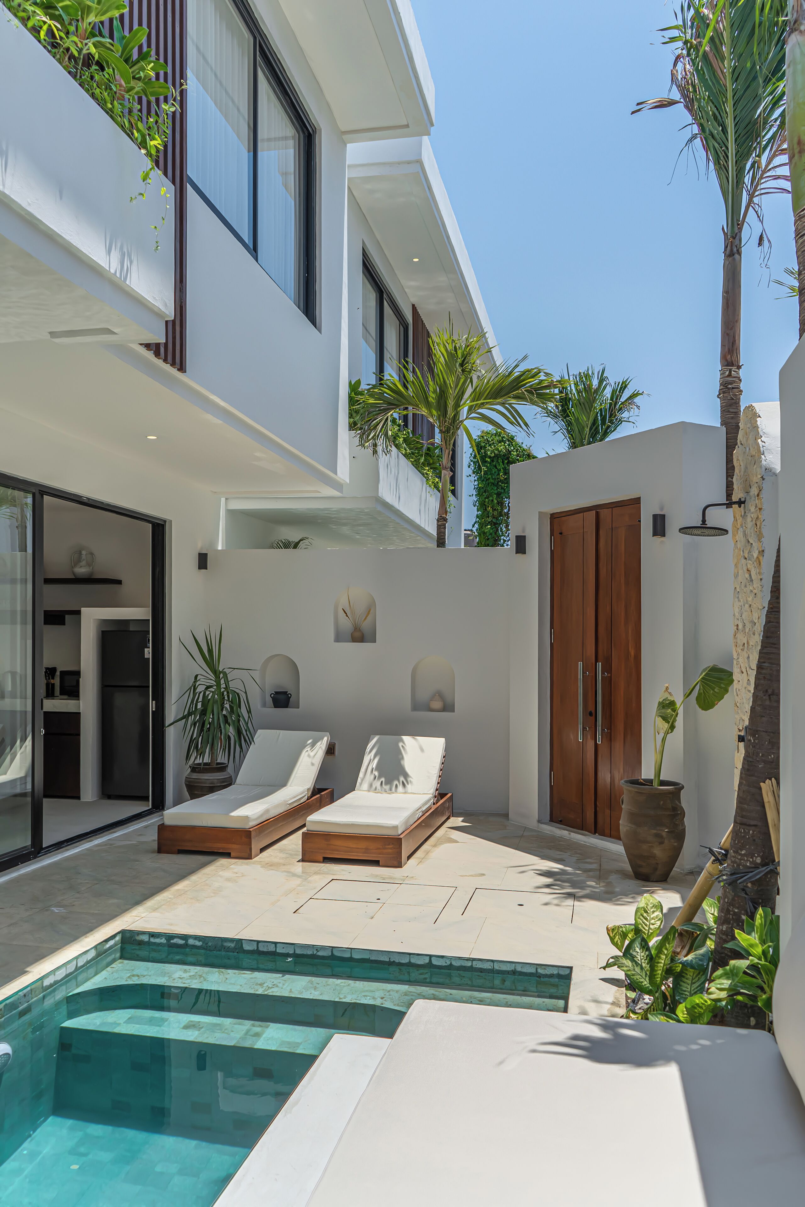 A modern outdoor pool area with two lounge chairs, a wooden door, and potted plants.