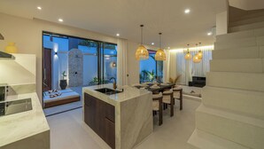 A modern kitchen with a large island, dining area, and a staircase. - Nova Oasis 3 (Canggu)