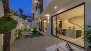 A modern house with a swimming pool, a dining area, and a kitchen visible through glass doors. - Nova Oasis 3 (Canggu)