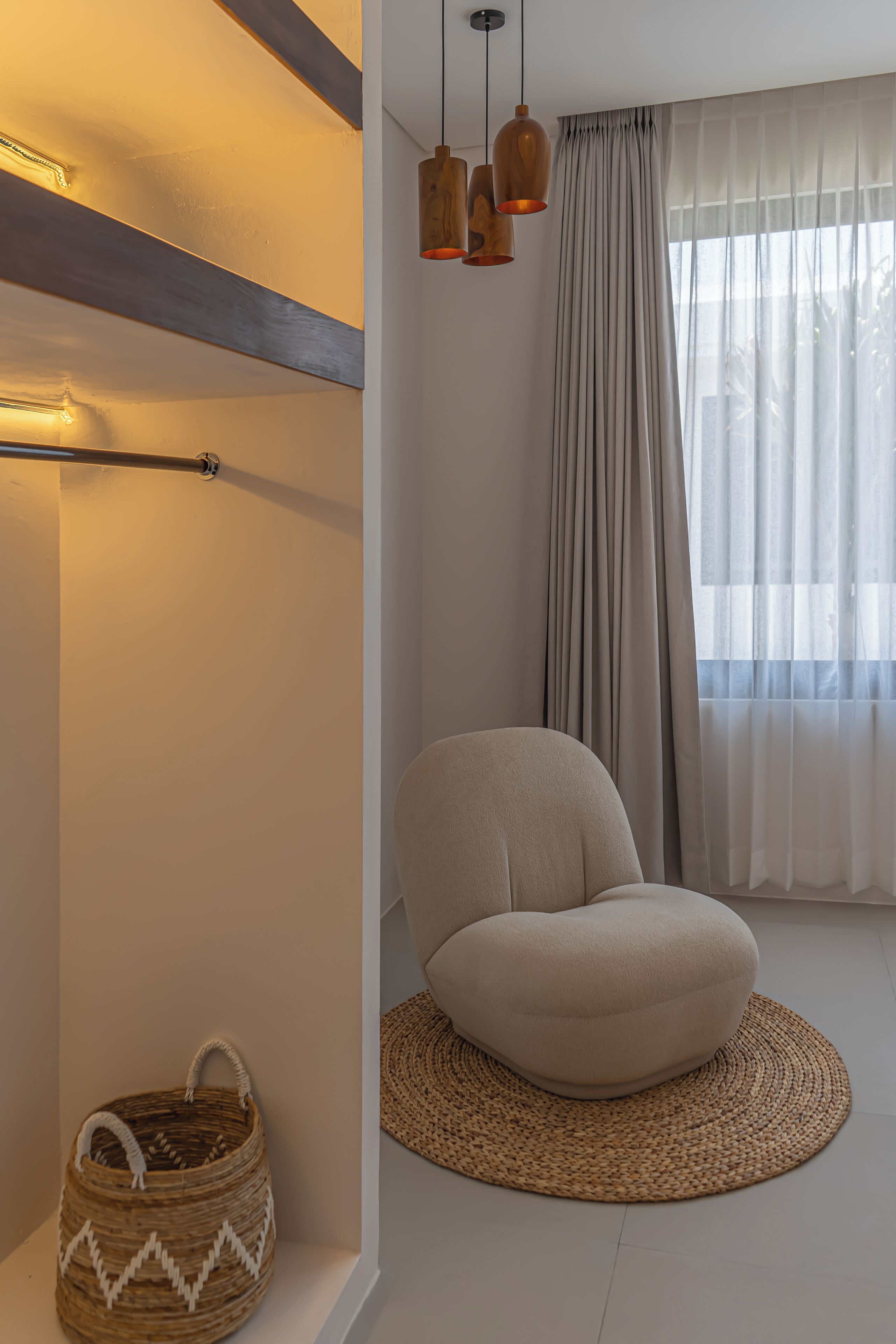 Una sala de estar moderna con una paleta de colores neutros, que incluye una butaca beige redondeada, una cesta tejida y un ventanal con cortinas traslúcidas.