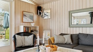 A cozy living room with a glass coffee table, a wicker chair, a grey sofa, and a bookshelf.