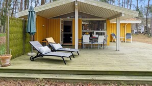 A wooden deck with lounge chairs, a covered patio, and a view of the surrounding forest.
