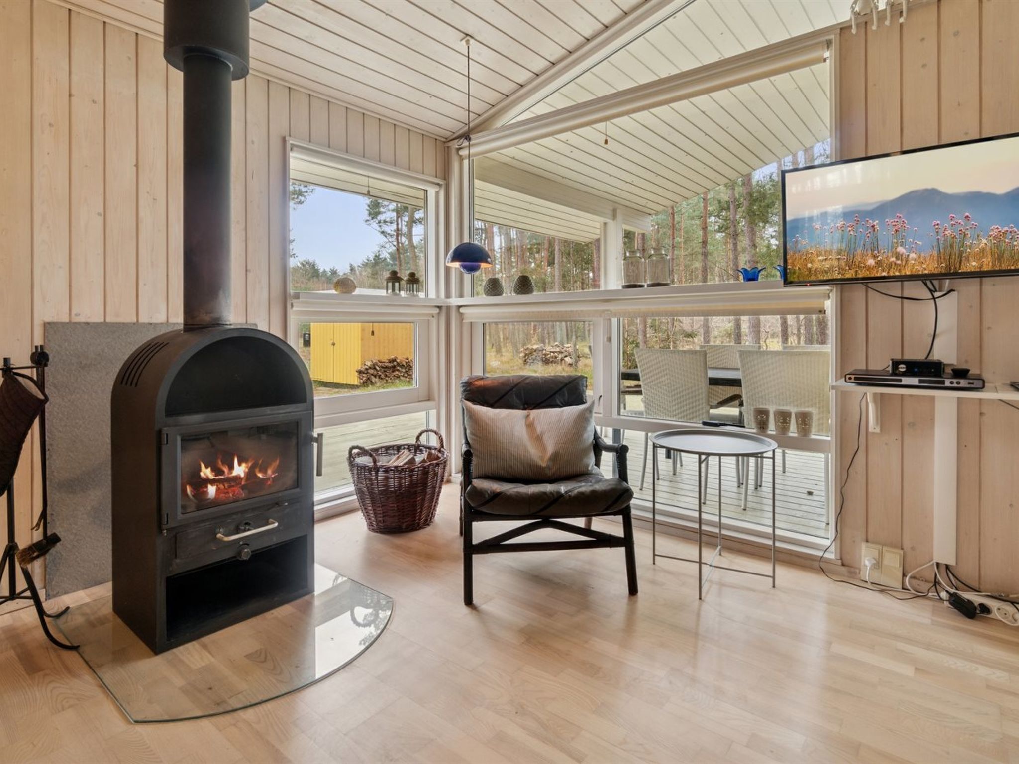 A cozy room with a wood-burning stove, wicker basket, comfortable seating, and a TV on a wall.