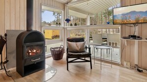 A cozy room with a wood-burning stove, wicker basket, comfortable seating, and a TV on a wall.