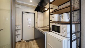 A compact kitchen with a microwave, rice cooker, and stacked appliances on shelves. - New Normal Condo in KENCHOMINAMIGUCHI (Naha)