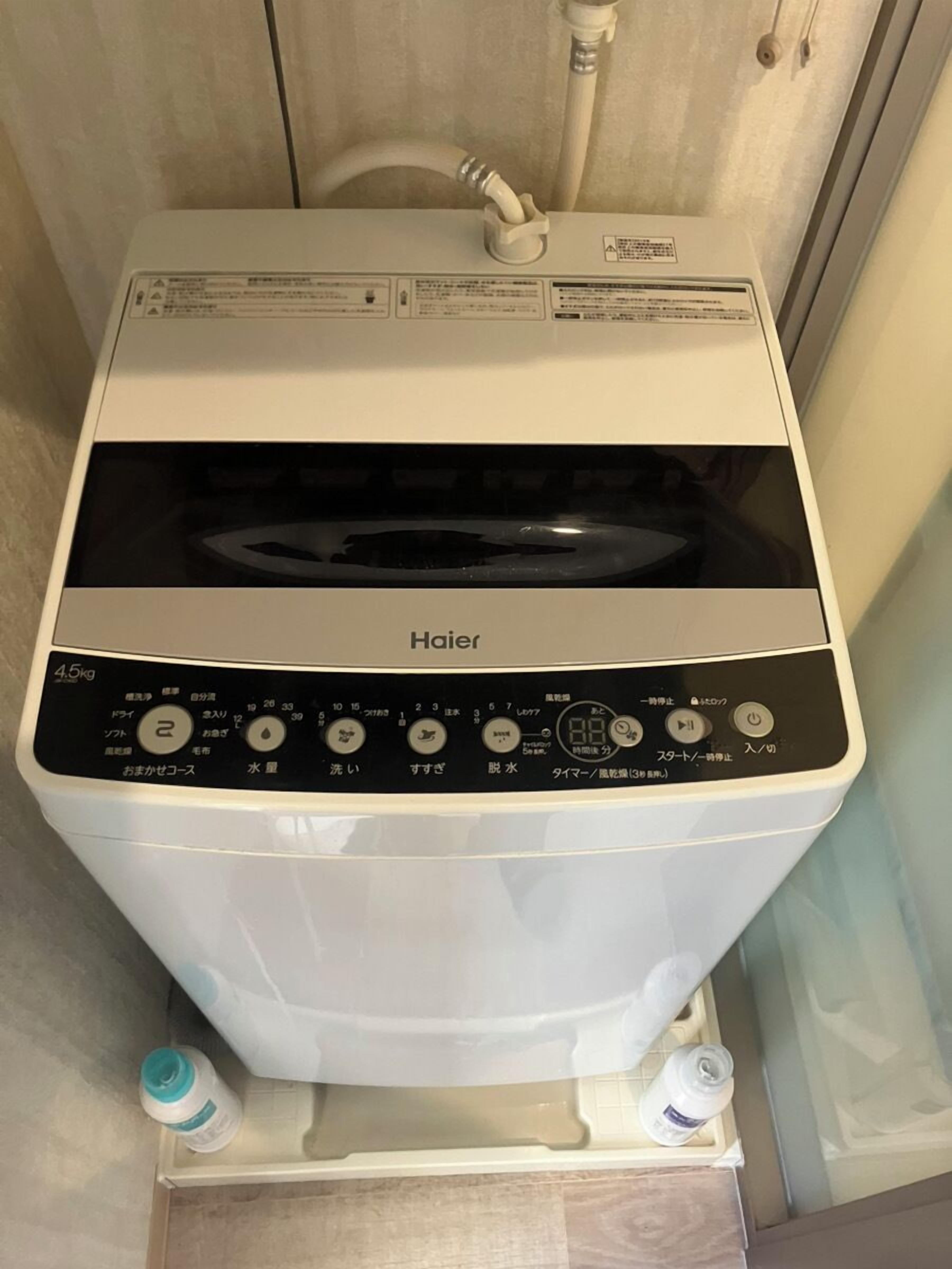 Una lavadora Haier en un baño con un panel de control, entrada de agua y dos botellas de agua.