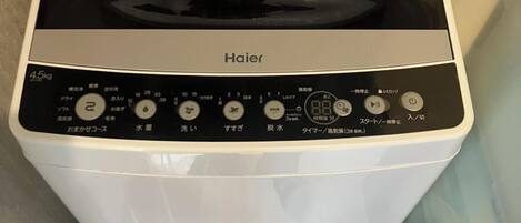 Una lavadora Haier en un baño con un panel de control, entrada de agua y dos botellas de agua.