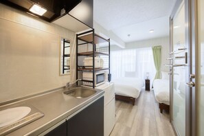 A compact hotel room with a kitchenette, a bed, a glass shower enclosure, and a view of the city. - New Normal Condo in KENCHOMINAMIGUCHI (Naha)