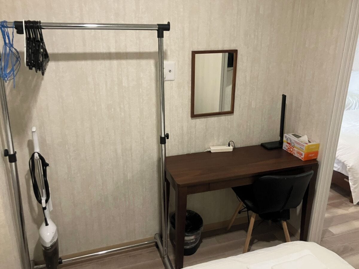 A small room with a desk, chair, and a standing shower.
