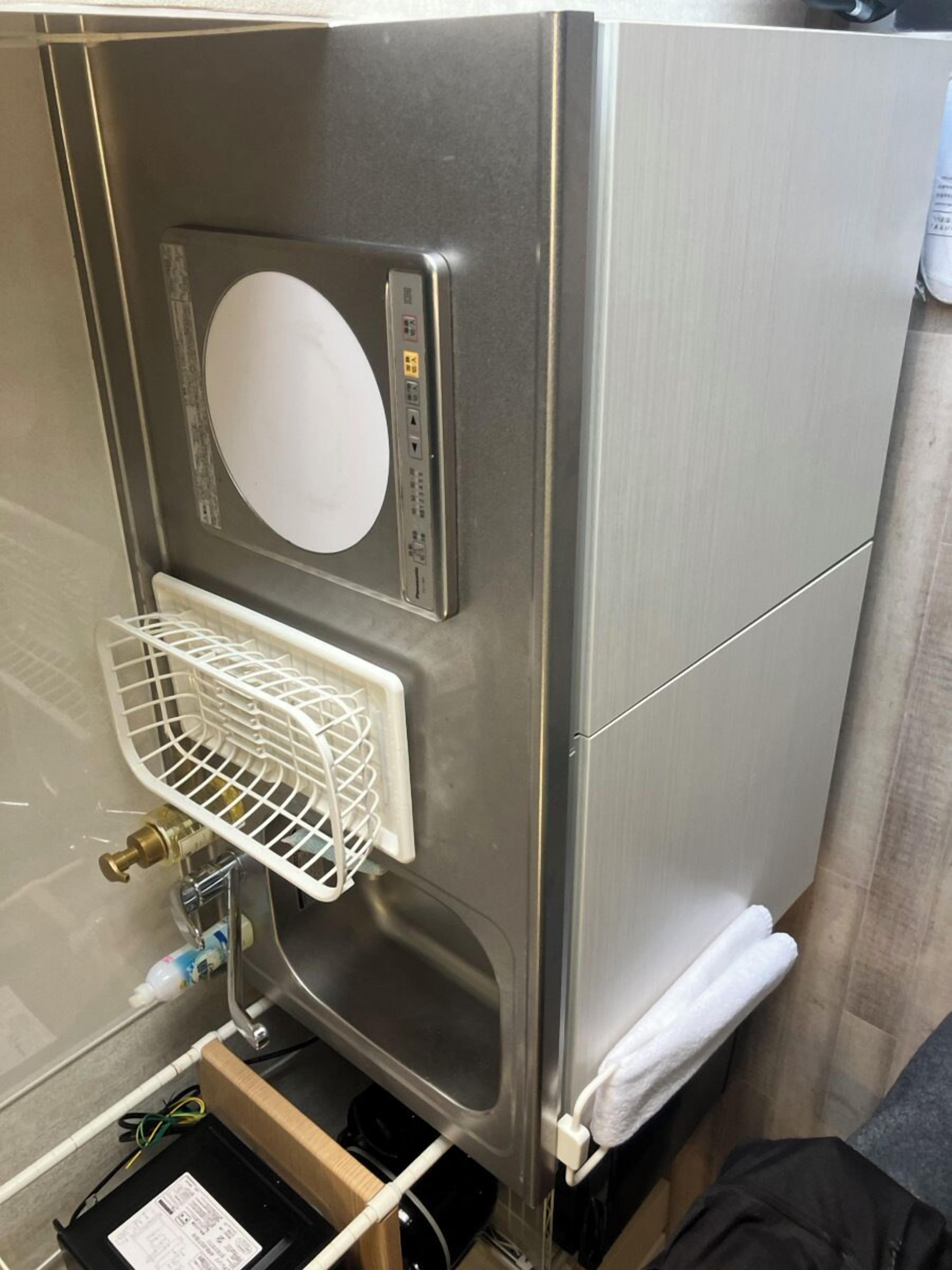 Een compact keukenblok van roestvrij staal met een ingebouwde magnetron, een klein spoelbakje en een witte afdruiprek.