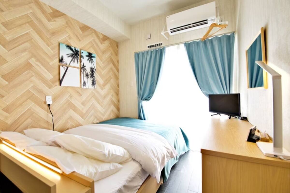 A hotel room with a bed, a desk, a TV, and an air conditioning unit.