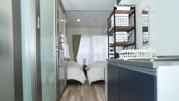 A compact hotel room with a bed, a small desk, a wardrobe, and a shower area. - New Normal Condo in KENCHOMINAMIGUCHI (Naha)