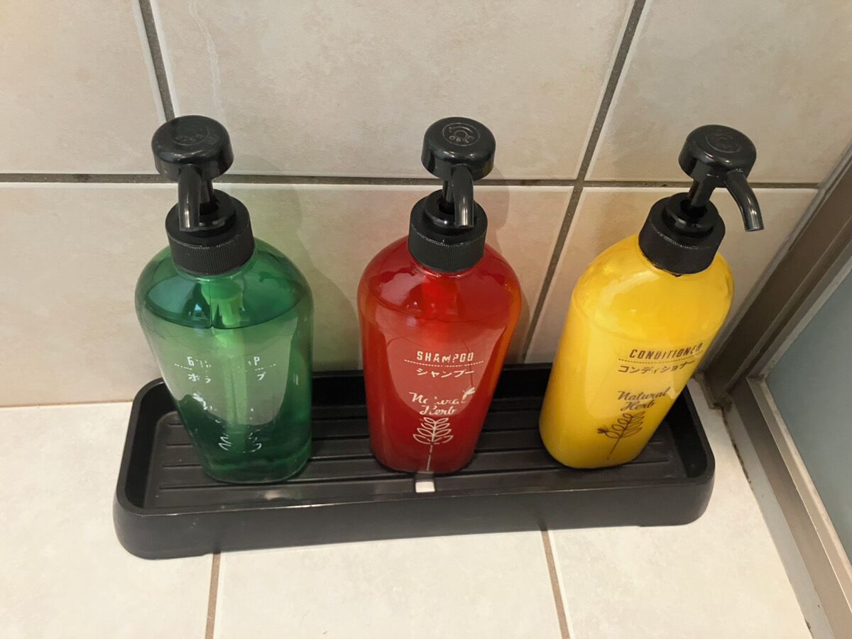 Three bottles of shampoo on a black tray in a bathroom.