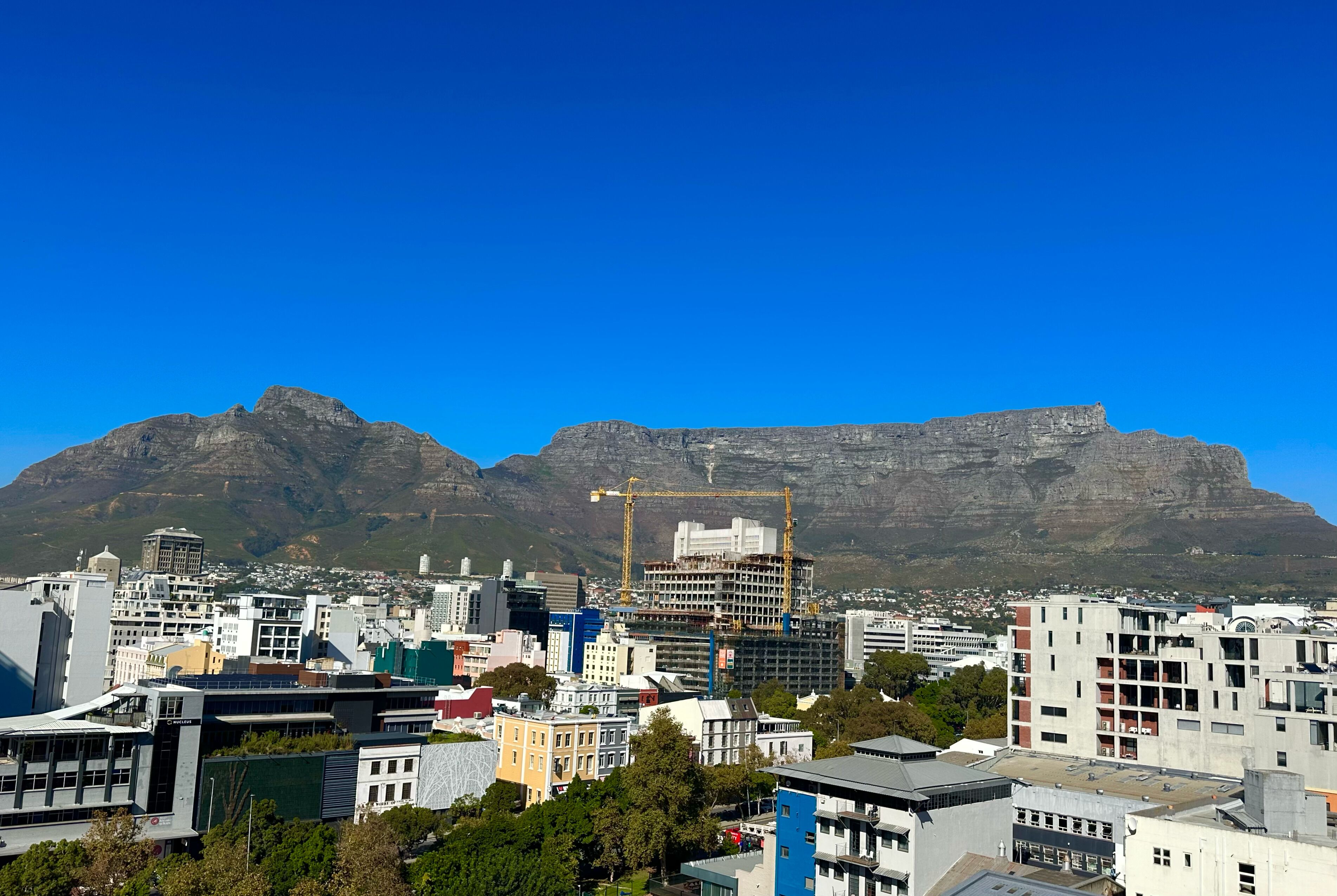 Un paisaje urbano con edificios modernos y una montaña destacada al fondo.